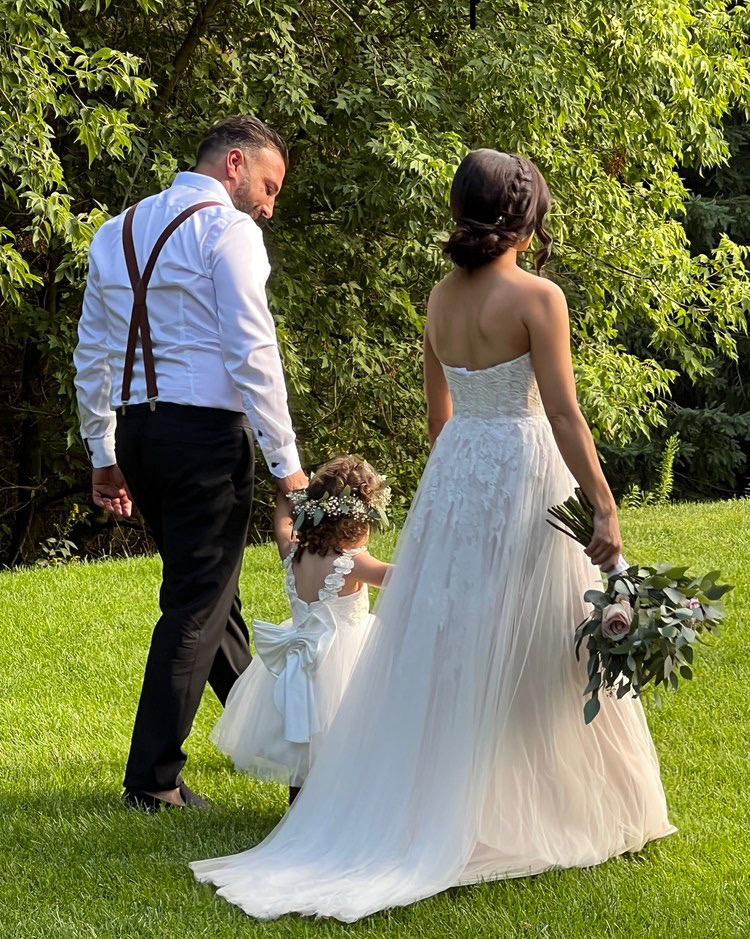 Bride walking away across grass with the flower girl, braided low updo pinned at the nape